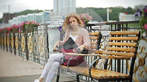 A girl using a smartphone on a bench in flowers on the beach, listening to music in headphones, dancing a yacht and