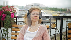 A girl using a smartphone on a bench in flowers on the beach, listening to music in headphones, dancing a yacht and