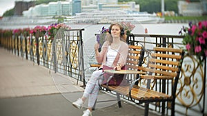 A girl using a smartphone on a bench in flowers on the beach, listening to music in headphones, dancing a yacht and