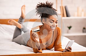 Girl Using Smartphone And Credit Card Lying In Bed Indoor