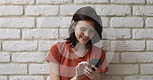 Girl using smartphone standing against white brick wall background
