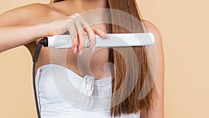 Girl using styler on her shining hair. Hairstyle. Woman ironing long hair with flat iron. Young woman straightening hair