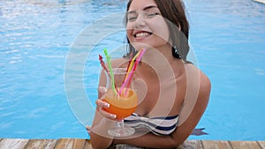 Girl on vacation by the pool happy young woman in bikini drinks vivid cocktail in blue water of pool