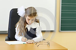 Girl in vest sits at teacher table and writes in
