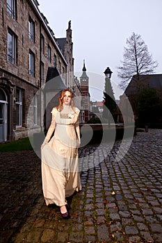 Girl in Victorian dress in a old city square in the evening walking