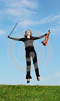 Girl with violin jumps on grass against sky