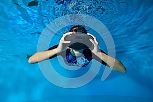 A girl in virtual reality glasses on her head swims underwater in the pool on a blue background. Close up. Underwater photography.