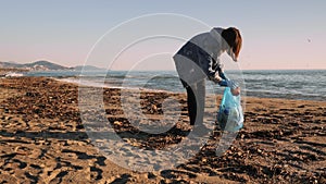 Girl volunteer picking up plastic bottles trash left on beach, keeping beach clean. Female collecting waste garbage on beach into