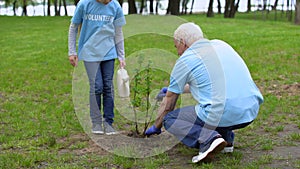 Girl volunteer watering can helping grandfather plant tree, smiling each other