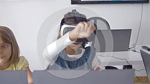 Girl in VR headset sitting at desk near classmate