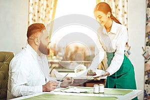 Girl waiter serves his dish in restaurant to a man