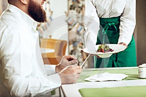 Girl waiter serves his dish in restaurant to a man