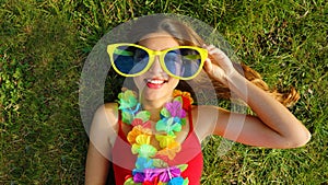 Girl wake up lying on grass after Carnival party. Panoramic banner view of young woman with carnival garland holds big funny