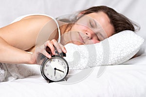 Girl wakes up in the morning. Young woman lying in bed in the morning. She is waking up with an alarm clock