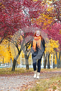 Girl walk on pathway in city park with red trees, fall season
