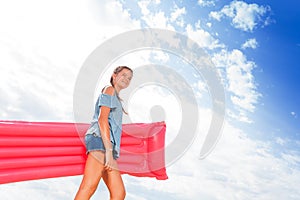 Girl walk with pink inflatable matrass to the sea