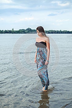 Girl walking alone in the water and holding her dress