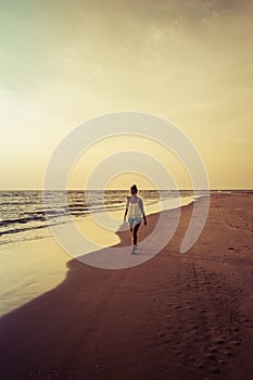 Girl walking along the beach at sunset