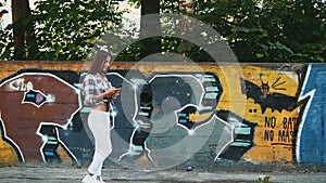 The girl is walking along the graffiti wall background. Copy space. 4K.