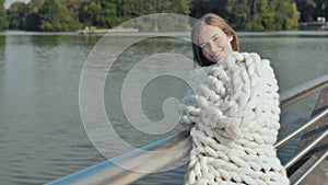 The girl is walking around the city lake, wrapped in a white plaid of merino wool in the early autumn.