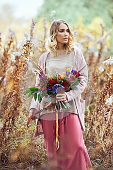 Girl walking in the autumn forest. A large beautiful bouquet of flowers in the hands of a woman. Girl stands in yellow red grass,