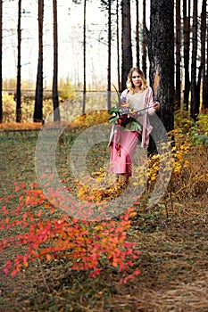 Girl walking in the autumn forest. A large beautiful bouquet of flowers in the hands of a woman. Girl stands in yellow red grass,