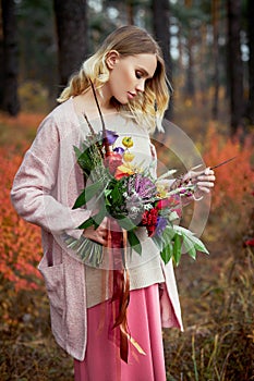 Girl walking in the autumn forest. A large beautiful bouquet of flowers in the hands of a woman. Girl stands in yellow red grass,