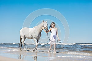 Girl walking on the beach with white horse.