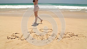 Girl walking in front of words I love summer written in sand on beach