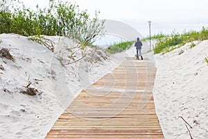 Girl walking on new light brown planks boardwalk in white sand d