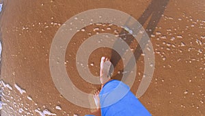 Girl walking on sandy beach. Sea ocean wave with white foam rolls on feet