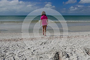Girl walking towards the ocean on a white sand beach