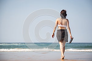 Girl walking towards the sea with flip flops in her hands