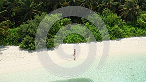 Girl walking on white beach on tropical island resort in Maldives