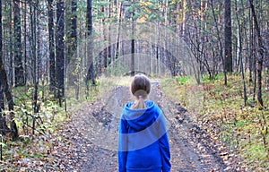 A girl walks alone while walking through the forest on an autumn day. Loneliness and melancholy. A young girl in a blue