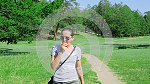 A girl walks along a country road in a green field and eating apple