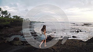 Girl walks along the rocks on the breathtaking coast at sunset, Bali in slow motion