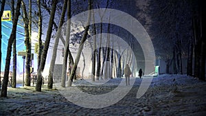 A girl walks along the sidewalk on a winter evening during a snowfall, a snow storm, cars drive along the road