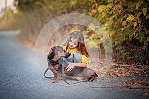 A girl walks through an autumn flogging with a dachshund dog. Child petting his dog