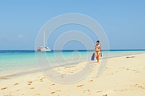 Girl walks on the beach with snorkelling gear with catamaran in