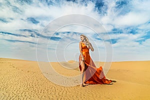 Girl walks on desert. Beautiful woman is walking, staing on sand or dune, touches, shows her legs. Blonde lady in