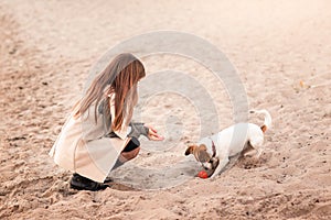 A girl walks with a dog on the banks of the river, the sea. The dog is playing with a ball.