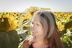 A girl walks through a field of sunflowers, looks inside a flower, looks tenderly, smiles.