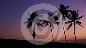 Girl walks through palm at sunset