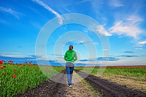 Girl walks on road surrounded with poppy fields