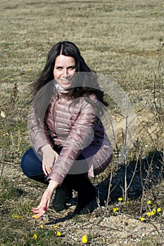 A girl walks through the spring park. Squatted down. Touching a flowering mother and stepmother