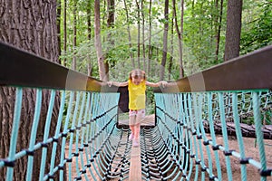 A girl walks on a suspension bridge at a children`s playground in the park