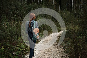 A girl walks in the woods along the road, a frame from the back from the side.