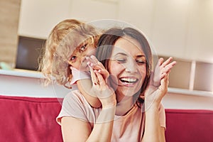 Girl wanna have fun. Young mother with her little daughter in casual clothes together indoors at home