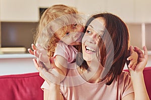 Girl wanna have fun. Young mother with her little daughter in casual clothes together indoors at home
